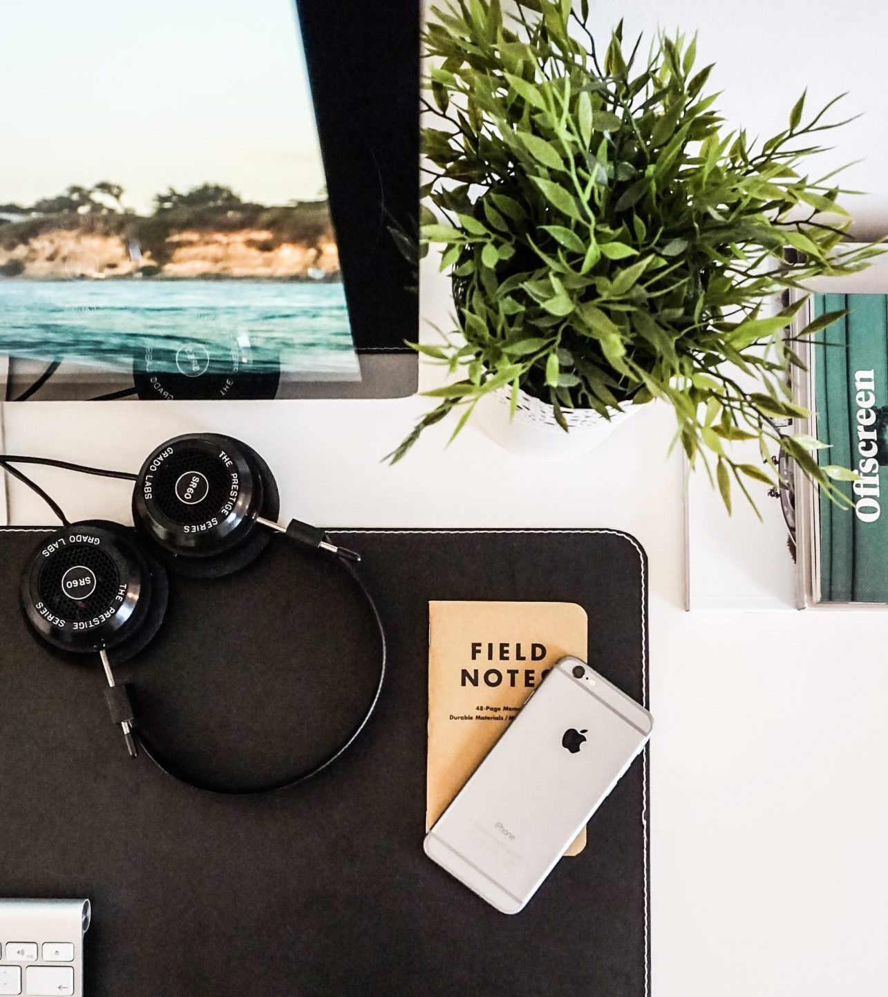 Computer, headphones, notebook, iPhone, and plant on top of white desk
