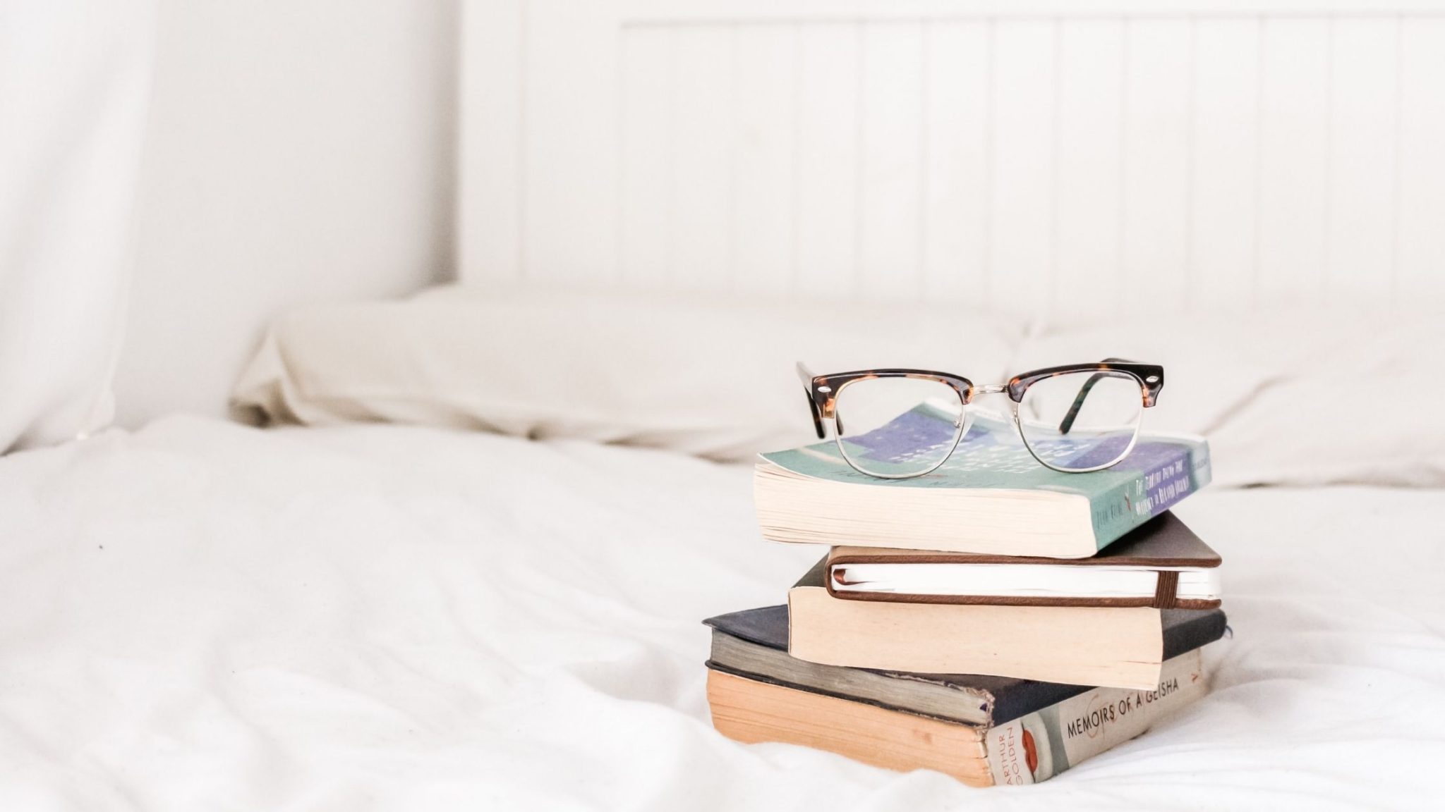 White bed with stack of books with glasses sitting on top